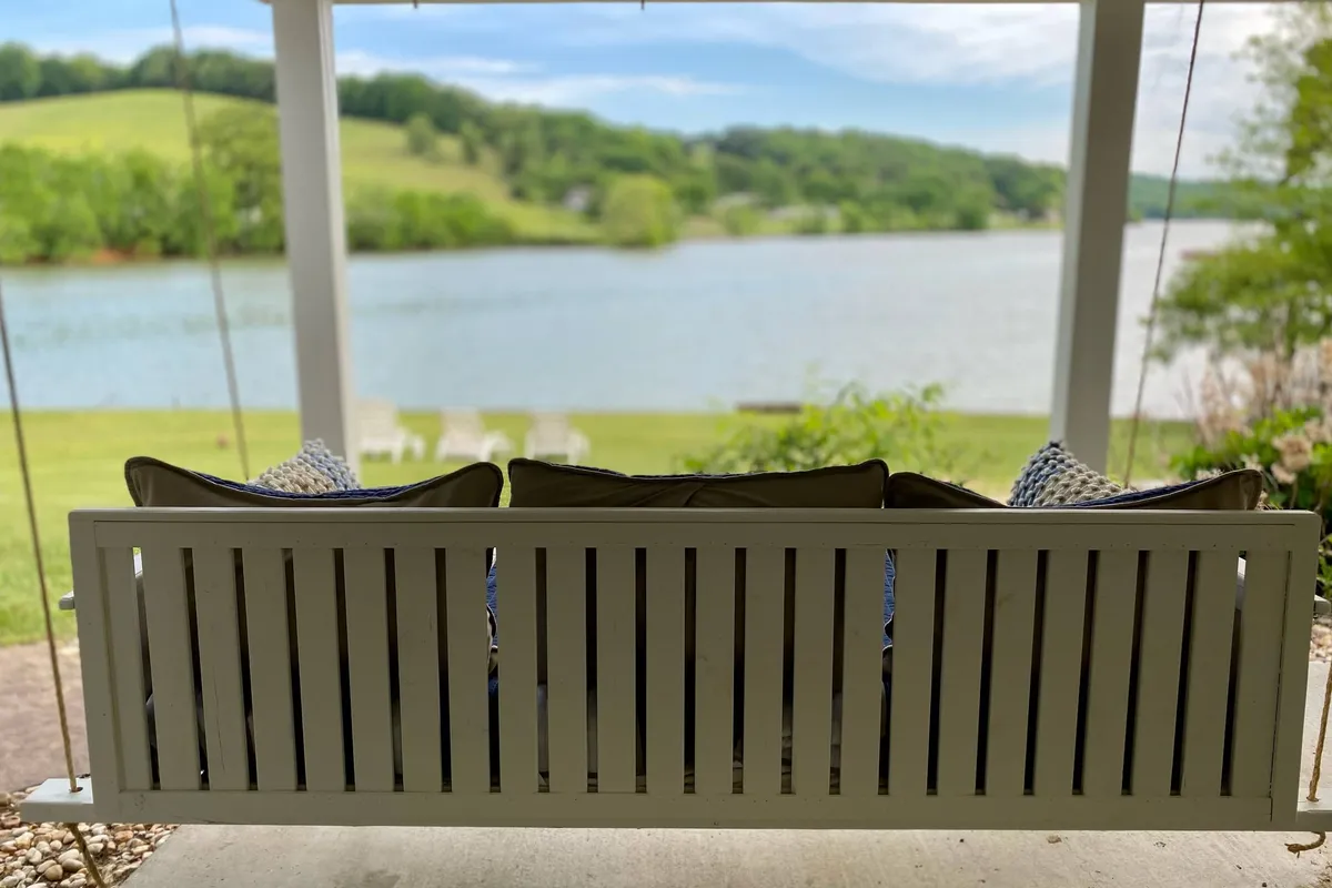A cozy swing bench overlooks the lake, with green hills rolling in the background. The inviting scene suggests peaceful moments spent reading, swinging, or relaxing while enjoying the lakeside view—a nod to both family downtime and multi-generational relaxation.