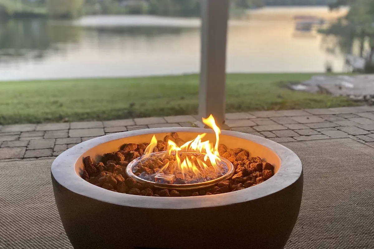 A cozy fire pit area with comfortable seating positioned to enjoy both the warmth of the fire and a wide view of the lake. The sun is setting in the background, lending a magical glow to the scene and inviting guests to relax and share moments outdoors.