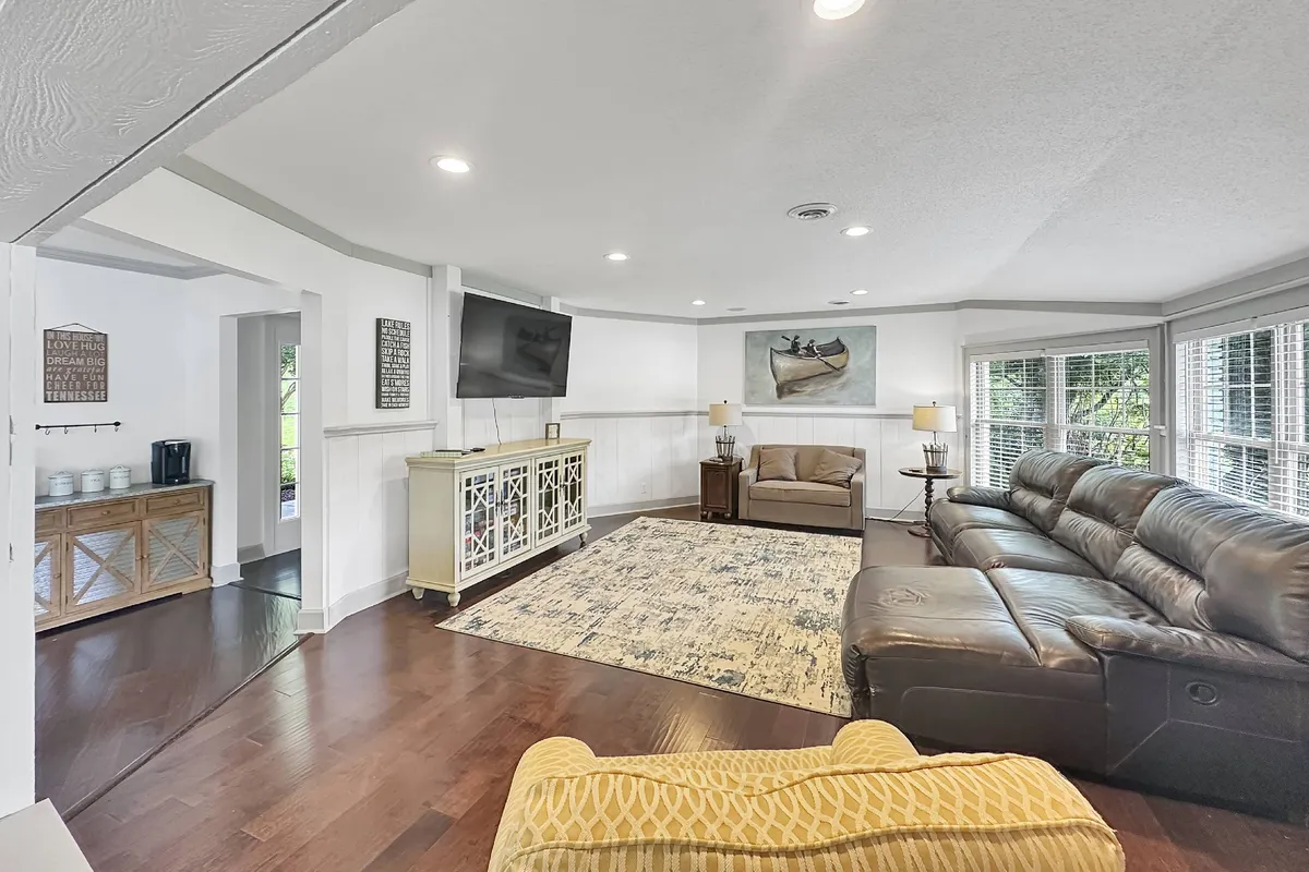 A comfortable, spacious living area featuring a leather sectional sofa, large area rug, mounted television, tasteful artwork, and side tables with lamps. The arrangement invites both conversation and relaxation, making it ideal for family gatherings, movie nights, or board game sessions.