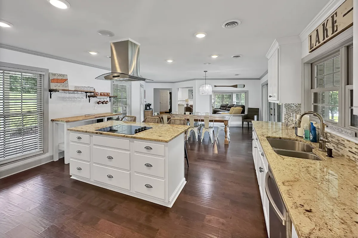 An open kitchen with a granite-topped island flows seamlessly into a dining area. The scene is bathed in natural light from large windows, highlighting the breakfast bar and spacious layout. The kitchen is fully equipped, making it ideal for shared meal preparation and gatherings.
