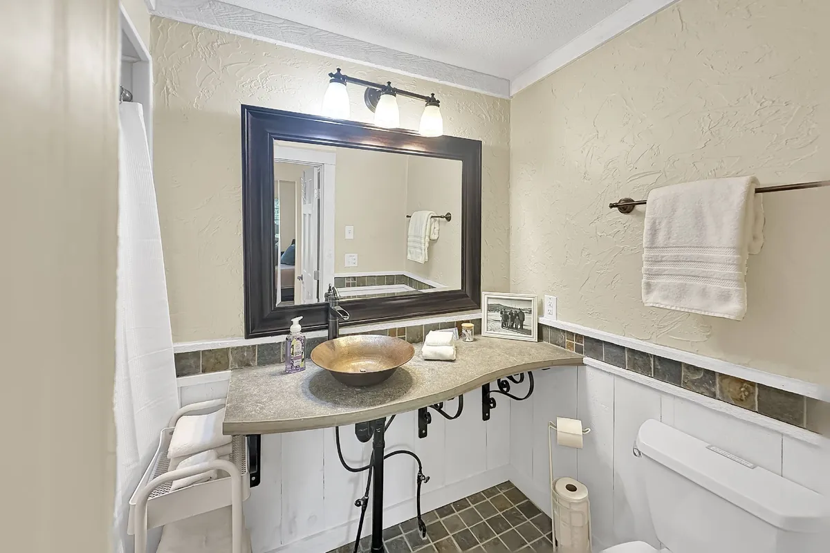 An elegant and functional bathroom scene featuring a decorative mirror, unique vessel sink, and a wall-mounted towel rack. The space is serene and well-appointed, suggesting guest convenience and a touch of spa-like comfort.