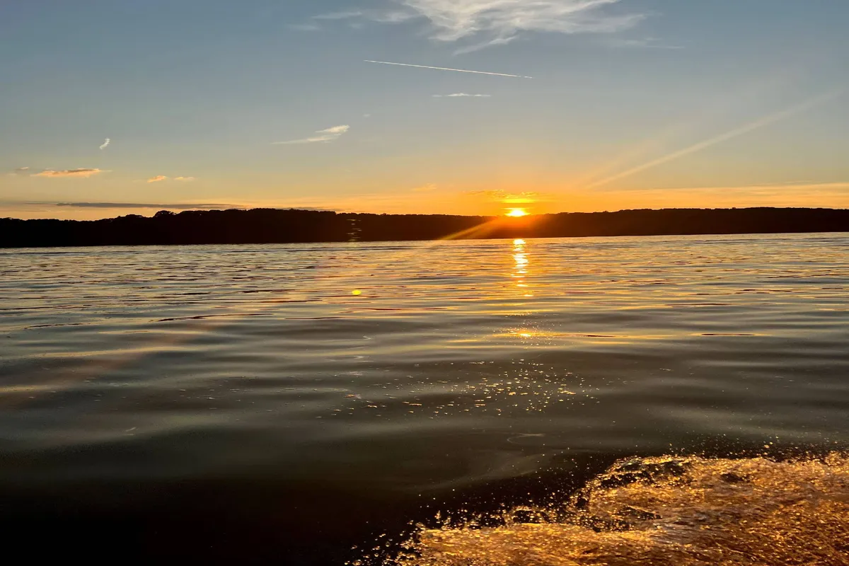 A tranquil lakeside scene at sunset, featuring calm water reflecting the colors of the sky. The horizon stretches peacefully, suggesting opportunities for boating and fishing. The setting evokes a sense of relaxation and connection to the water, with ample space for water-based activities.