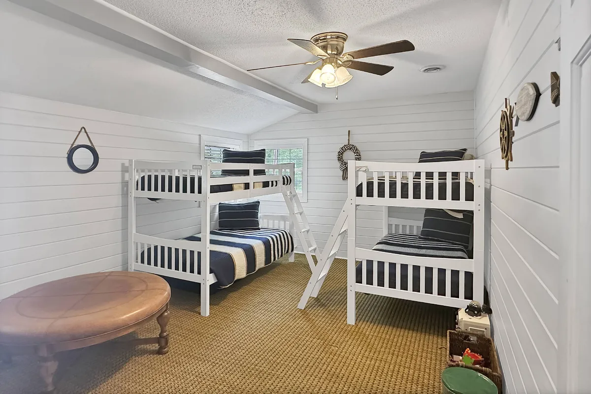 A cheerful, kid-friendly bunk room with two bunk beds, a ceiling fan, and a round wooden table, evoking a playful and inviting atmosphere. Ideal for group sleepovers and after-adventure hangouts, the space is bright and designed for fun.