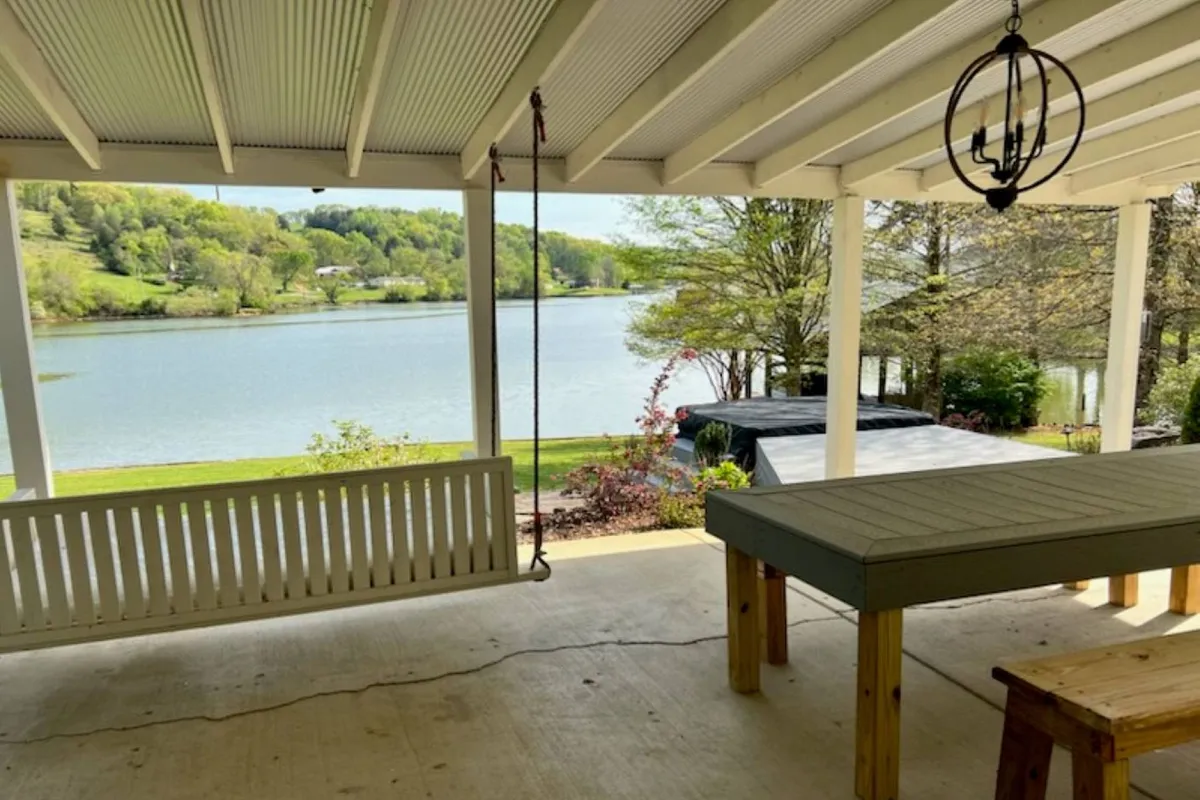 An exterior view featuring a serene lake backdrop, an outdoor table, and a swing. The setting exudes relaxation and provides a beautiful backdrop for outdoor play and socializing.